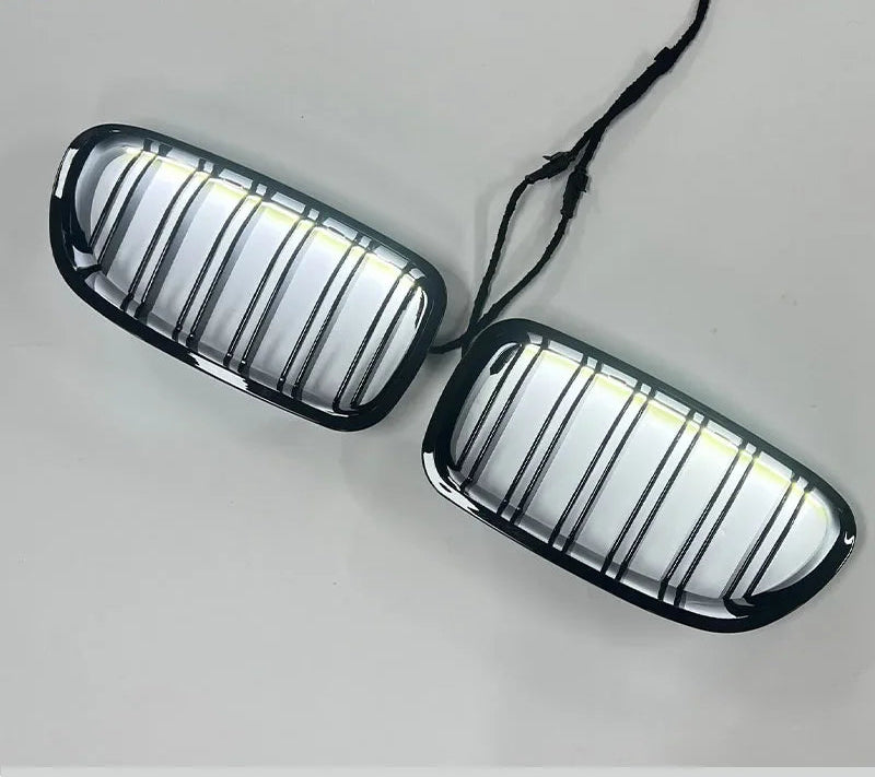 Paire de calandres BMW noir brillant avec LED, vue en angle sur fond clair