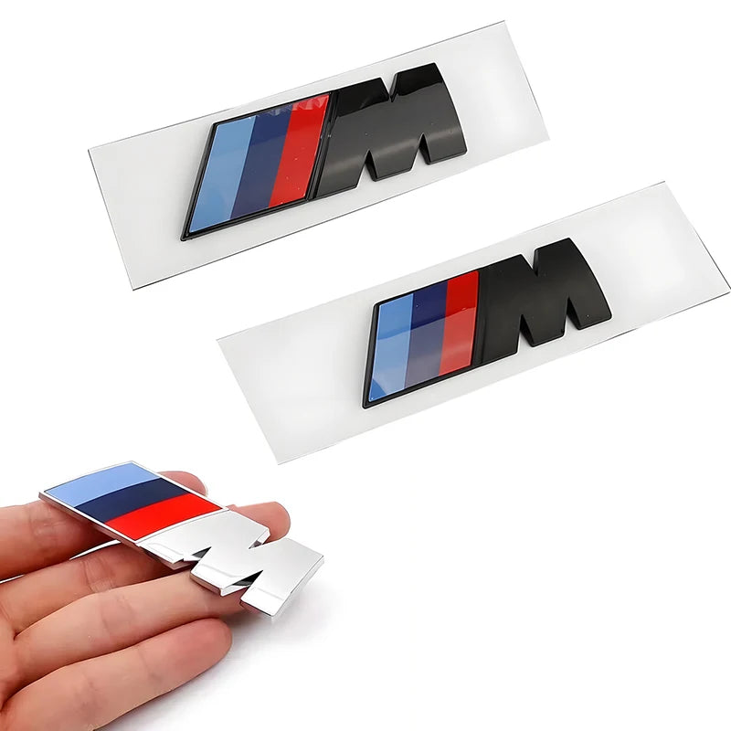 Deux logos BMW M Performance posés sur leur support avec un logo tenu en main pour montrer l’épaisseur