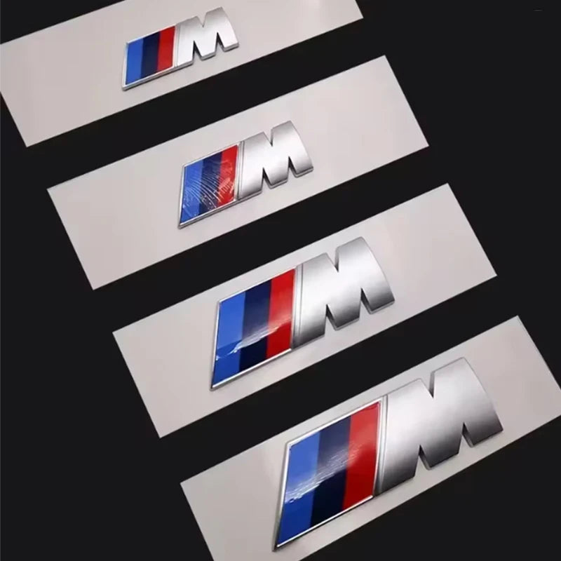 Plusieurs logos BMW M Performance alignés sur fond noir pour montrer les différentes tailles disponibles